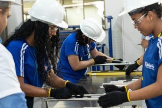Alunos do SENAI em treinamento com capacetes e óculos de proteção em um laboratório.