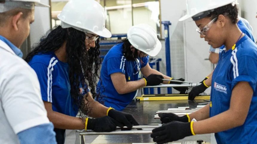 Alunos do SENAI em treinamento com capacetes e óculos de proteção em um laboratório.