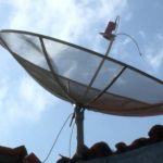 Antena parabólica tradicional no telhado sob céu azul com nuvens
