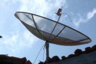 Antena parabólica tradicional no telhado sob céu azul com nuvens