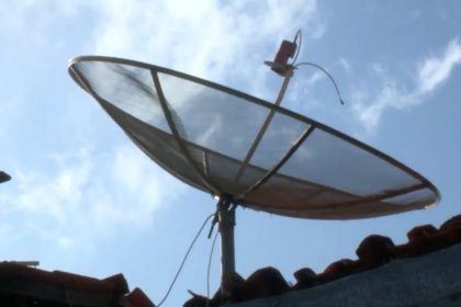 Antena parabólica tradicional no telhado sob céu azul com nuvens