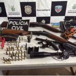 Apreensão de armas e munições em Itacoatiara, Amazonas. Pistola, espingardas, binóculos e cartuchos sobre uma mesa.