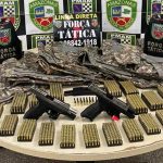 Apreensão de armas, munições e coletes da Polícia Militar em mesa.