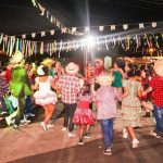 Arraial com dança folclórica em festa junina, com pessoas vestidas a caráter e decoração festiva.