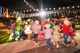 Arraial com dança folclórica em festa junina, com pessoas vestidas a caráter e decoração festiva.