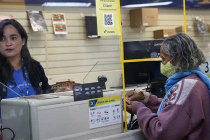 Atendimento em agência dos Correios: funcionária atende cliente com máscara