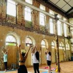 Aula de yoga em um espaço com estrutura antiga, com pessoas praticando exercícios.