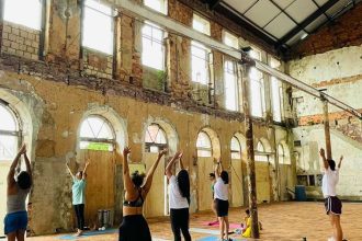 Aula de yoga em um espaço com estrutura antiga, com pessoas praticando exercícios.