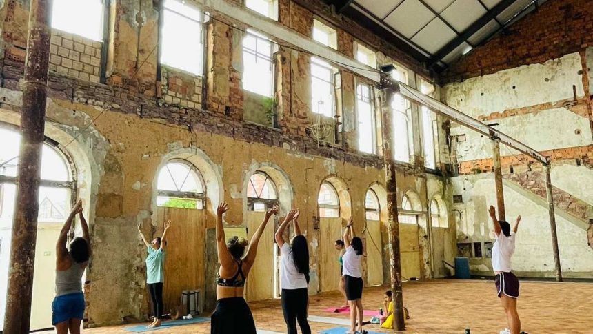 Aula de yoga em um espaço com estrutura antiga, com pessoas praticando exercícios.