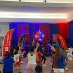 Aulão de Boi Bumbá no Shopping Ponta Negra, com pessoas dançando e banda no palco.