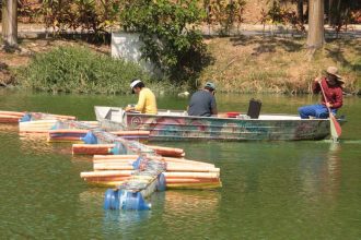 Barcos no lago: imagem de três pessoas em um barco, próximo a estruturas flutuantes e margem.