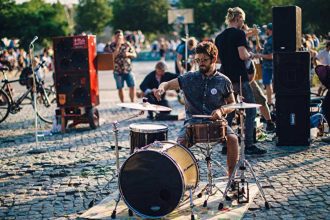 Baterista tocando ao ar livre em evento musical, com público ao fundo.