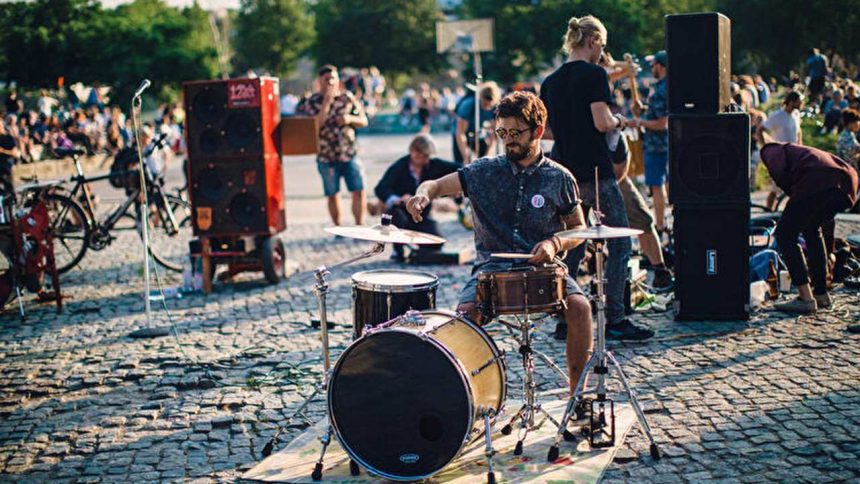 Baterista tocando ao ar livre em evento musical, com público ao fundo.