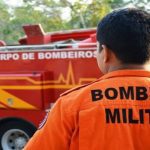Bombeiro militar em frente a um caminhão do corpo de bombeiros.