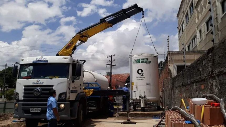 Caminhão Dunloc com guindaste içando tanque de oxigênio líquido White Martins.