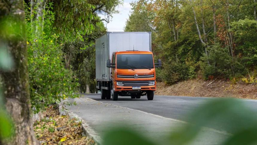 Caminhão laranja Volkswagen Delivery em estrada arborizada.
