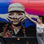 Cantora Cella posando ao lado de um ônibus com sua imagem promocional.
