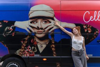 Cantora Cella posando ao lado de um ônibus com sua imagem promocional.