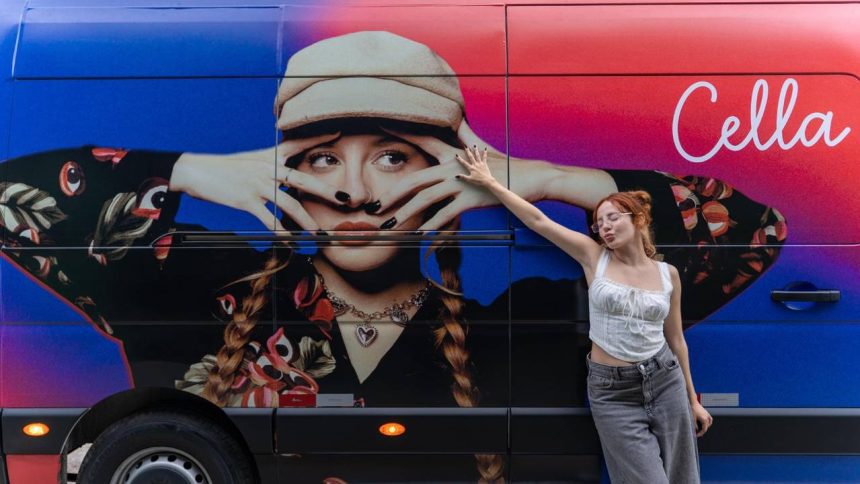 Cantora Cella posando ao lado de um ônibus com sua imagem promocional.