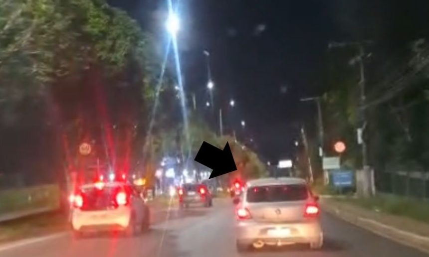 Carros em movimento na Avenida do Turismo à noite, com luzes vermelhas acesas.