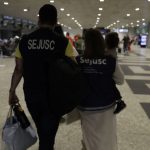 Criança reunida com a mãe em aeroporto, acompanhada por equipe da Sejusc.