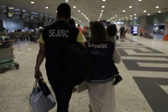 Criança reunida com a mãe em aeroporto, acompanhada por equipe da Sejusc.