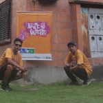 Dois homens em frente a um grafite, em um evento de arte de rua.