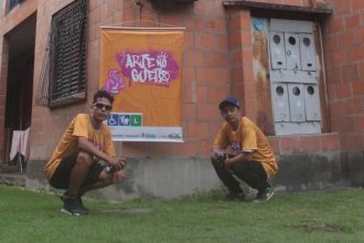 Dois homens em frente a um grafite, em um evento de arte de rua.