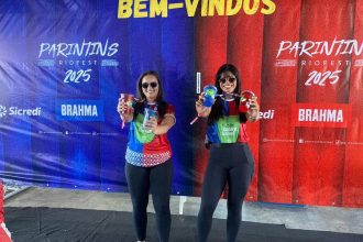 Duas mulheres segurando copos promocionais em evento da Sicredi Parintins.