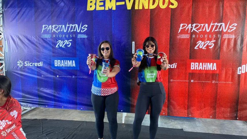 Duas mulheres segurando copos promocionais em evento da Sicredi Parintins.