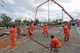 Equipe de construção civil trabalhando em obra de asfalto, usando equipamentos e uniformes laranja.