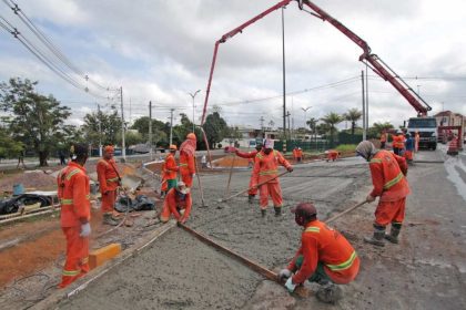 Equipe de construção civil trabalhando em obra de asfalto, usando equipamentos e uniformes laranja.