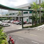 Estacionamento em frente à Tapajós Distribuidora, Manaus, com carros e passarela coberta.