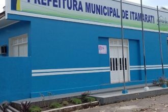Fachada da Prefeitura Municipal de Itamarati, em tom azul, com placa e mastros.