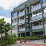 Fachada da sede da Fiocruz em Manaus, com árvores e céu azul.