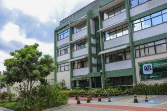 Fachada da sede da Fiocruz em Manaus, com árvores e céu azul.