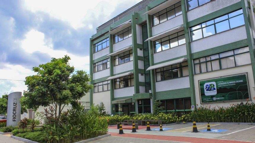 Fachada da sede da Fiocruz em Manaus, com árvores e céu azul.