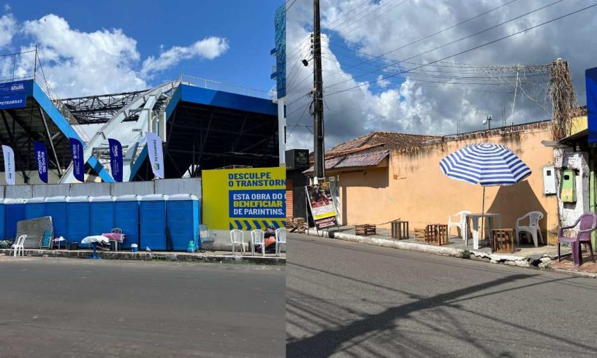 Fachada de estádio com banners e banheiros químicos, e rua com mesas e guarda-sol, em Parintins.