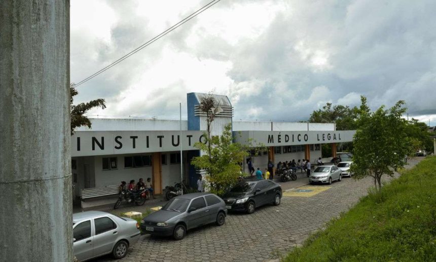 Fachada do Instituto Médico Legal (IML) com carros estacionados e pessoas na frente.