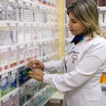 Farmacêutica manuseando medicamentos em prateleiras de farmácia.