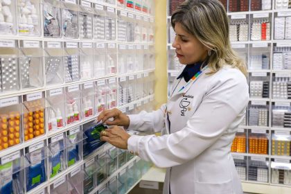 Farmacêutica manuseando medicamentos em prateleiras de farmácia.