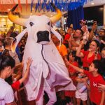 Festa com boi-bumbá em shopping, crianças e adultos interagindo.