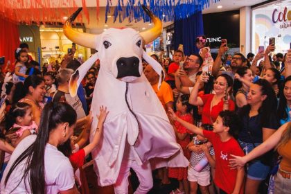 Festa com boi-bumbá em shopping, crianças e adultos interagindo.
