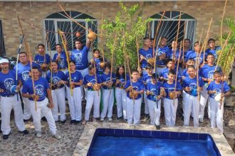 Grupo de capoeiristas em evento gratuito em Manaus, segurando berimbaus e vestindo azul e branco.