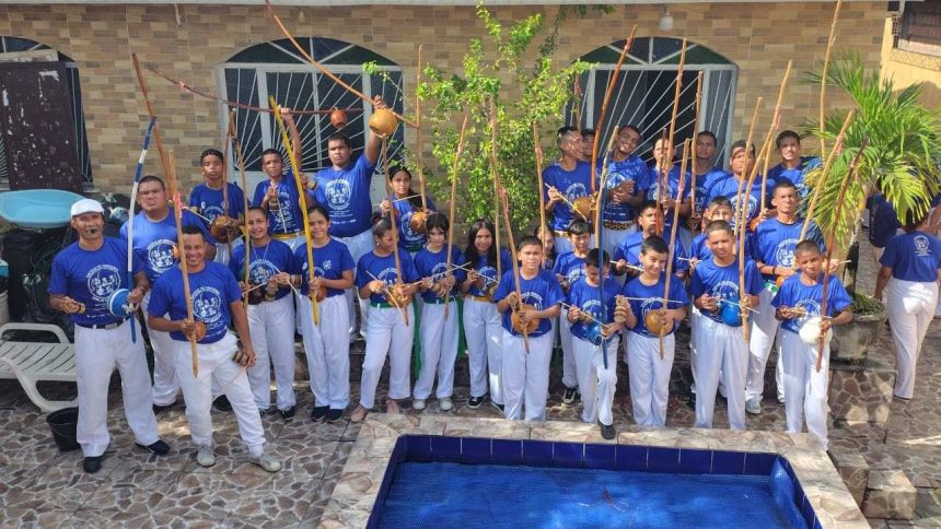 Grupo de capoeiristas em evento gratuito em Manaus, segurando berimbaus e vestindo azul e branco.