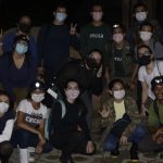 Grupo de pessoas com máscaras faciais em trilha noturna na floresta.