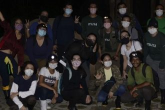 Grupo de pessoas com máscaras faciais em trilha noturna na floresta.