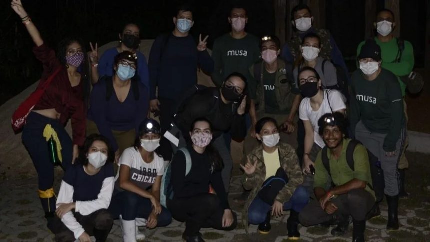 Grupo de pessoas com máscaras faciais em trilha noturna na floresta.