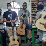 Grupo de pessoas com máscaras segurando violões em oficina.
