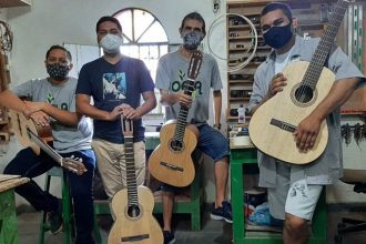 Grupo de pessoas com máscaras segurando violões em oficina.